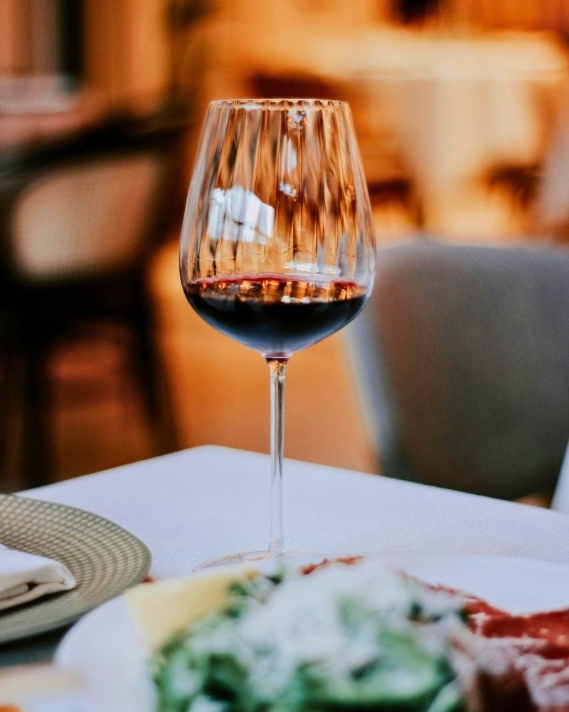 Glass of red non-alcoholic wine on a restaurant table, softly lit with a blurred dining background.