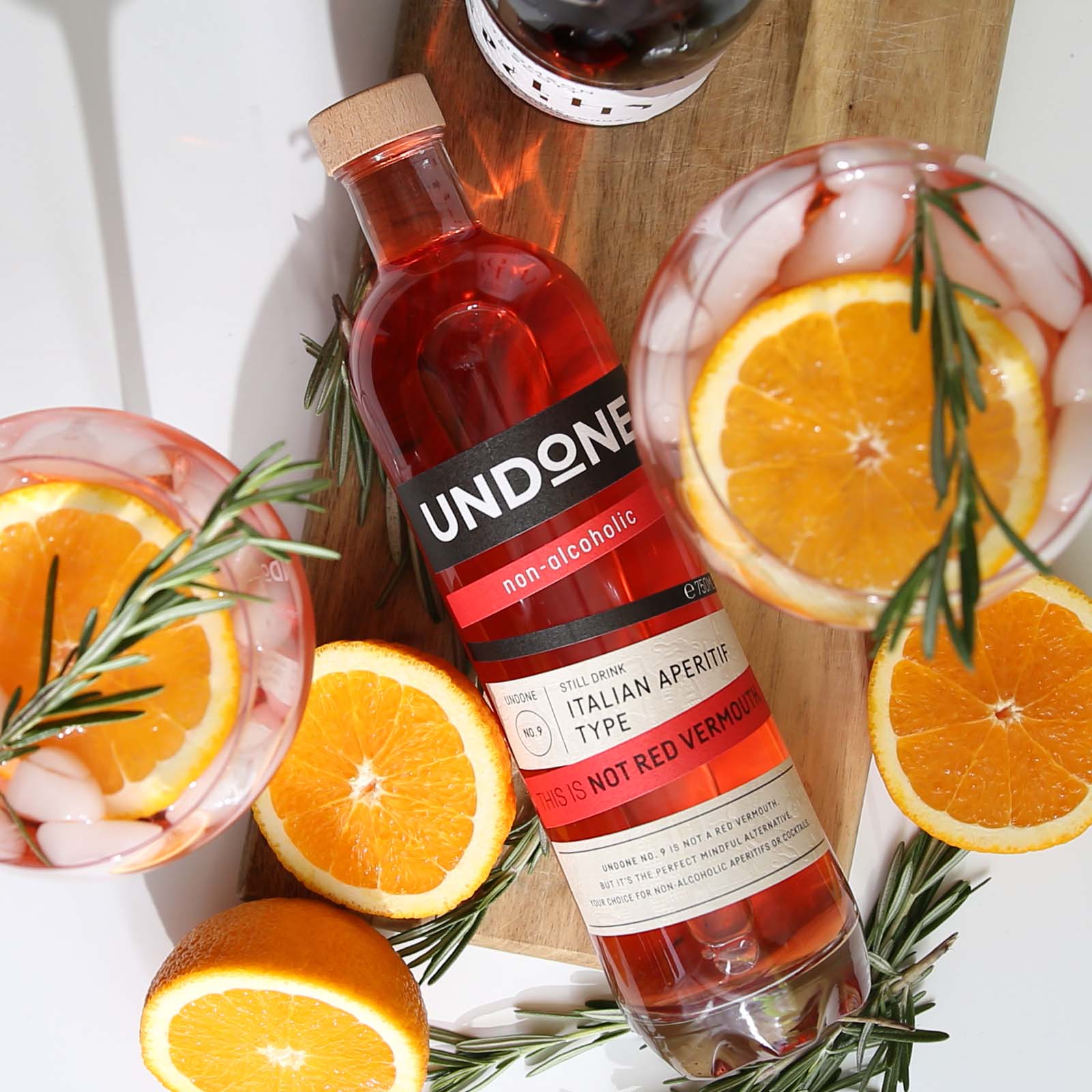 Bottle of Undone non-alcoholic spirits surrounded by two cocktail glasses and orange slices