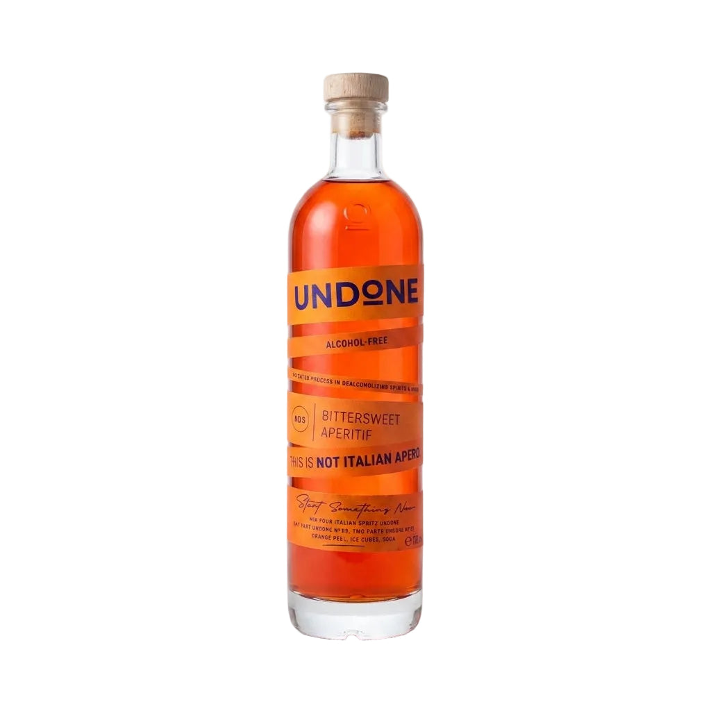 A bottle of Undone Alcohol Free Bittersweet Apetite non-alcoholic bitters, featuring a clear glass bottle filled with amber liquid, an orange label with blue text, and a light wood cap, set against a plain white background.