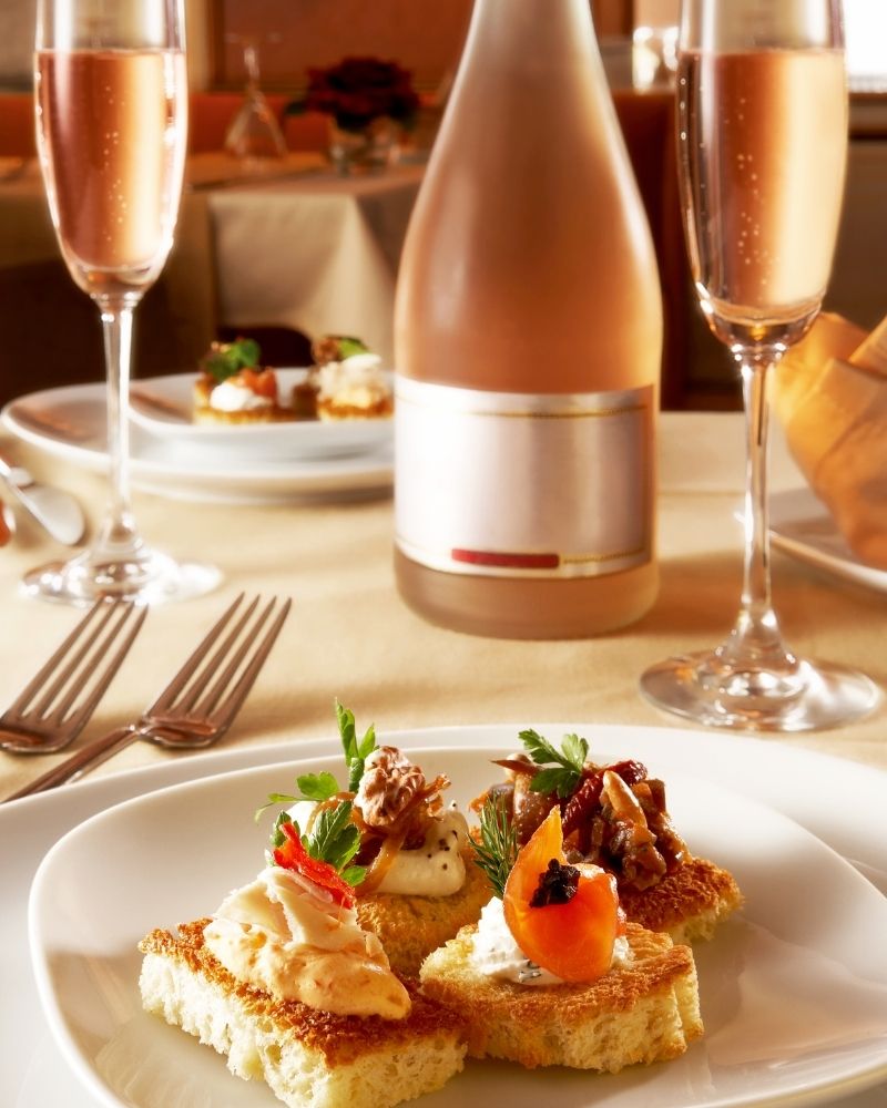 Brunch table with small plated dishes and glasses of pale sparkling non-alcoholic wine, styled in warm natural light.