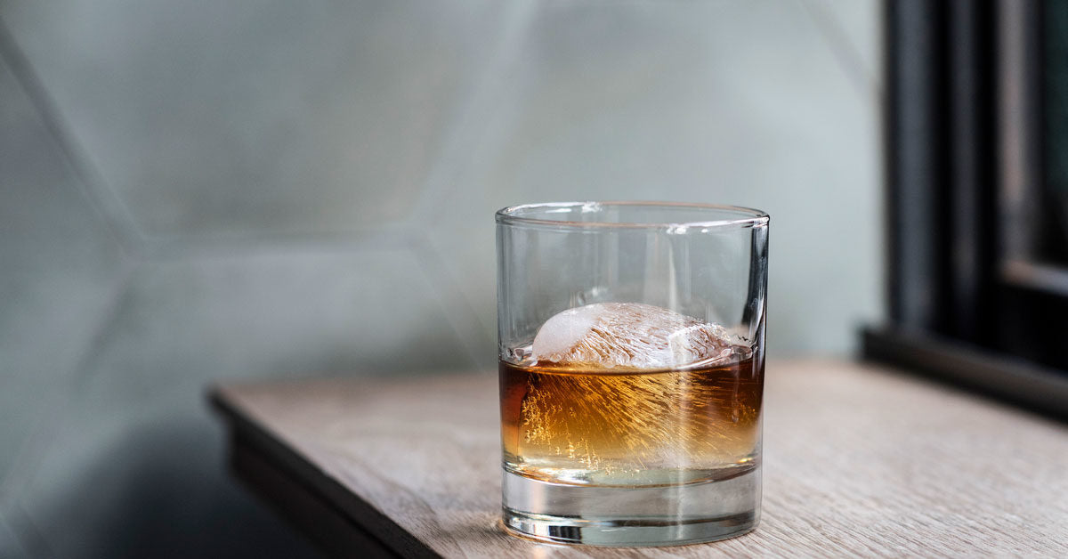 glass of non-alcoholic bourbon in a glass with large ice cube  