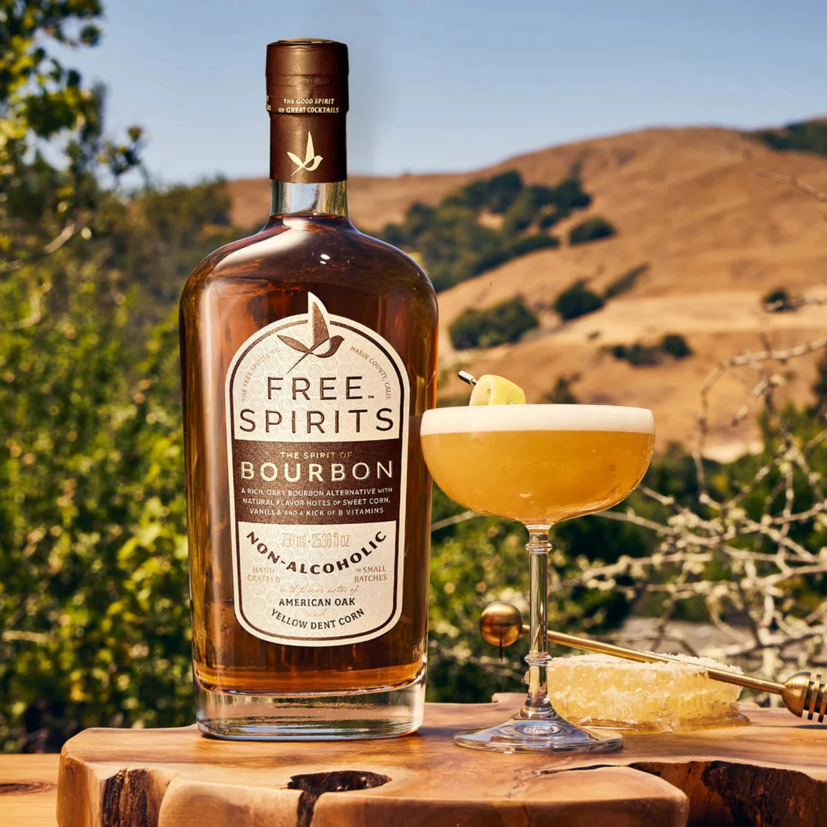 a bottle of free spirits bourdon on a live edge wooden table with desert mountains in backgroud sitting next to a Lemon Sour cocktail in a coupe glass