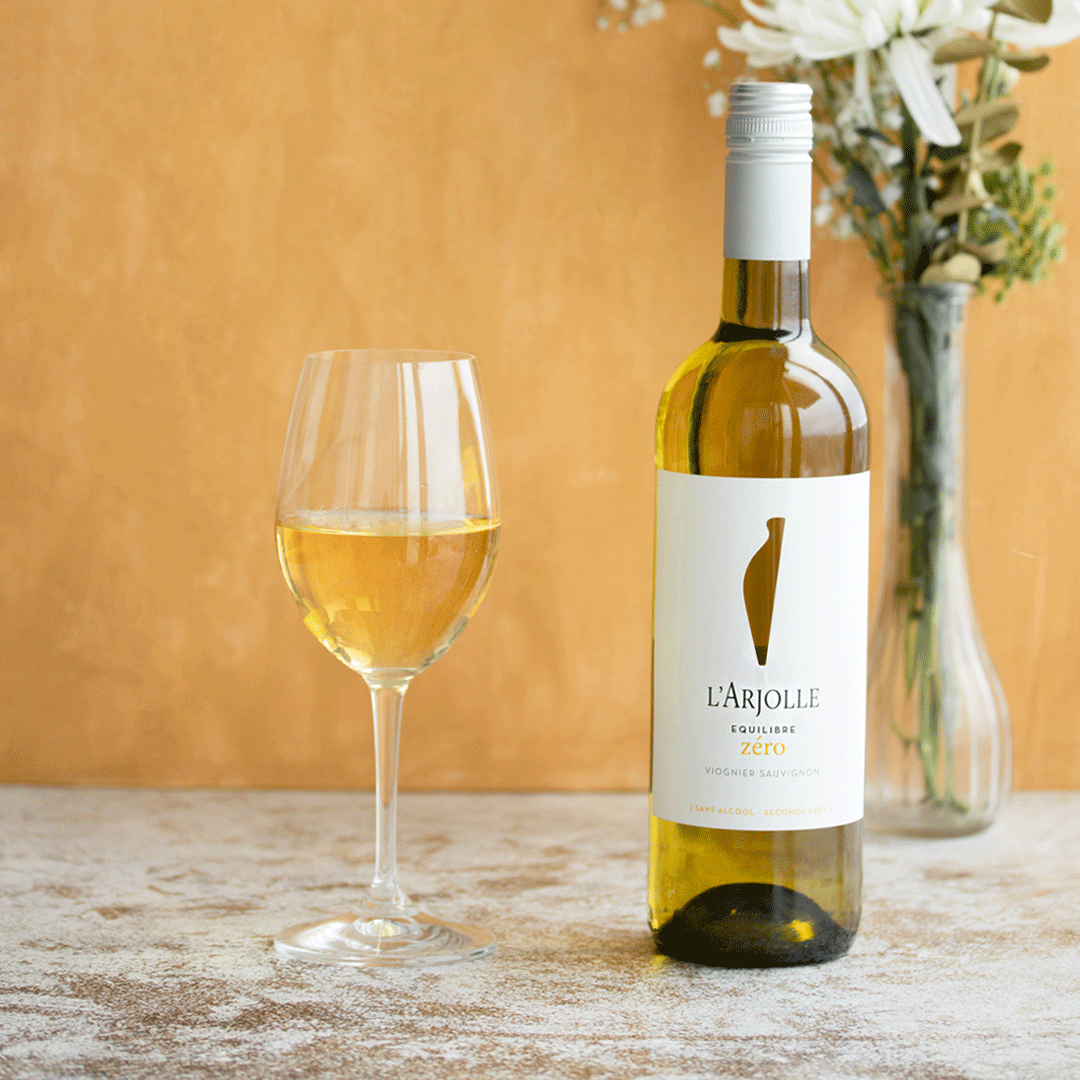 L’Arjolle Équilibre Zéro non-alcoholic Viognier Sauvignon Blanc with pale golden hue in glass beside the bottle.