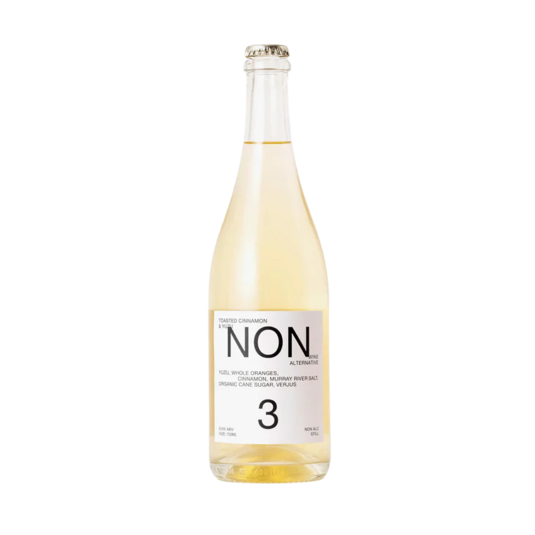 A bottle of NON 3 Toasted Cinnamon & Yuzu non-alcoholic beverage. The bottle has a clear glass design showcasing a pale golden liquid, with a minimalist white label displaying the brand name "NON" and flavor details like yuzu, whole oranges, cinnamon, and Murray River salt.