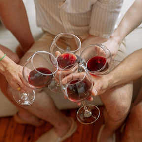 close up lifestyle photo of red wine in glasses toasting each other