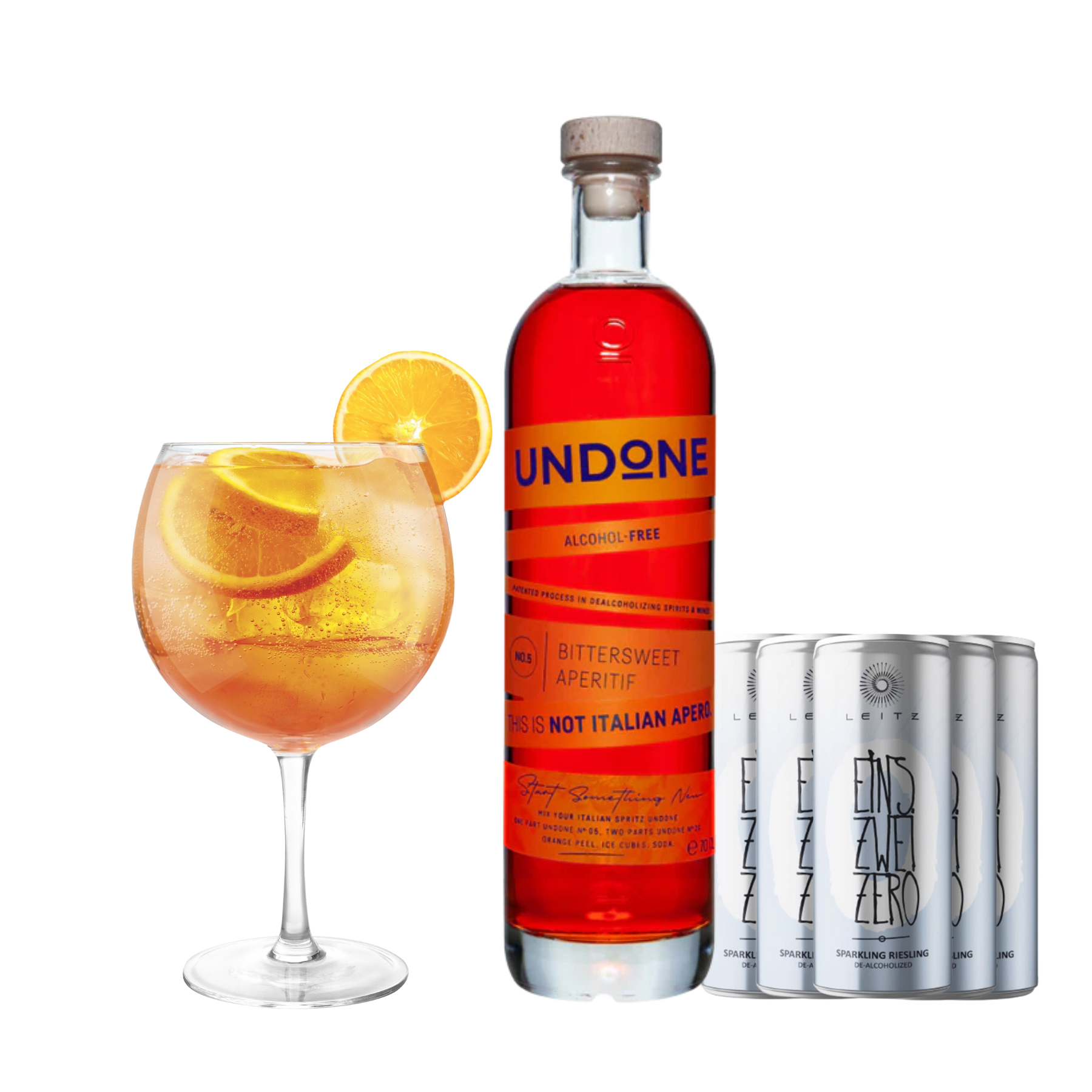 A non-alcoholic spritz cocktail bundle featuring a bottle of Undone No. 5 Bittersweet Aperitif, a set of Leitz Eins Zwei Zero Sparkling Riesling cans, and two large balloon glasses—one filled with an orange-hued spritz garnished with fresh orange slices. The aperitif bottle has a bold red-orange label with the text 'THIS IS NOT ITALIAN APERO' in uppercase letters